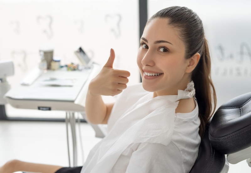 A happy woman in dental chair giving thumbs-up after dental implant procedure in Charles Town, WV