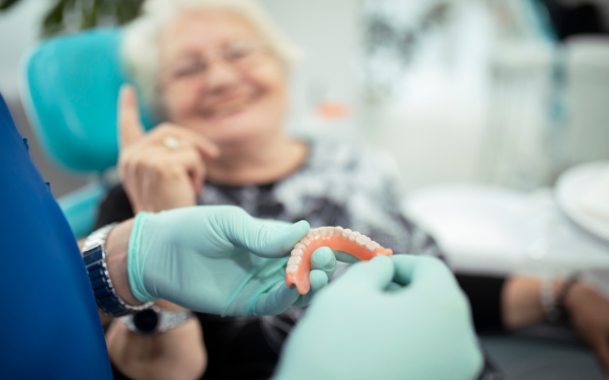 A dentist showing implant-supported dentures to a smiling elderly patient in Charles Town, WV