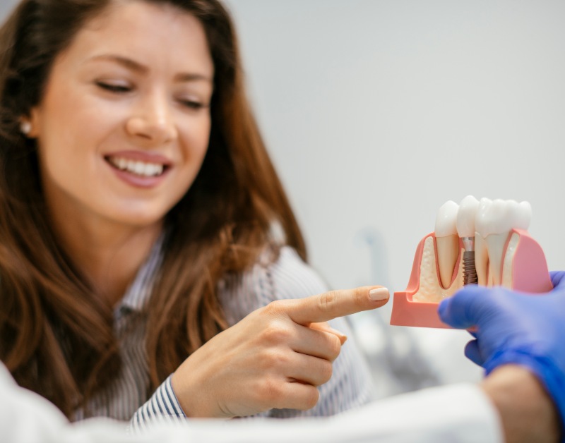 A dentist explaining dental implants with a model to a smiling patient in Charles Town, WV
